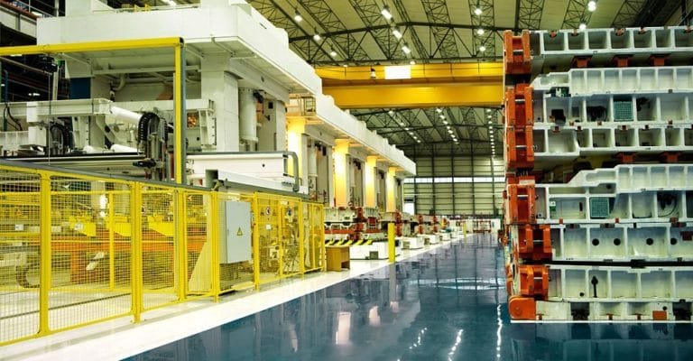 Industrial press machinery beside a reflective production aisle with yellow safety barriers