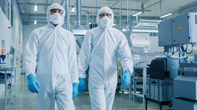 Two technicians in protective clothing beside machinery in a controlled industrial production area