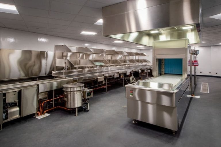 Commercial dishwashing area with stainless steel equipment, a grey floor and floor-drain grates
