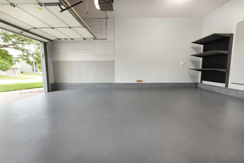 Grey coated garage floor beside an open garage door and dark wall shelving