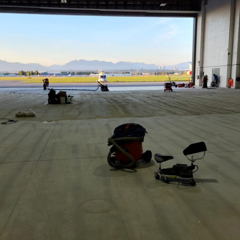 Mechanical concrete floor preparation inside the Million Air YVR hangar with aircraft visible outside
