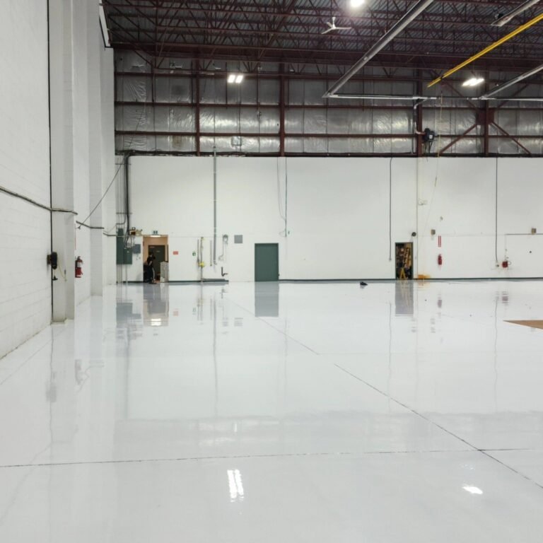 Overhead lighting reflected in the completed light-coloured resin floor inside the YVR hangar