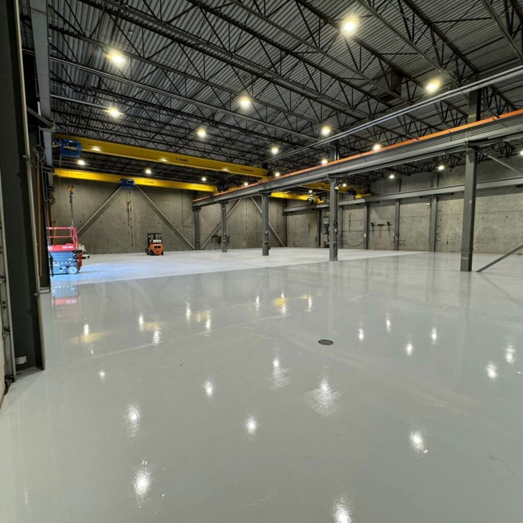 Light-grey epoxy floor beneath overhead cranes at the Liebherr facility in Abbotsford